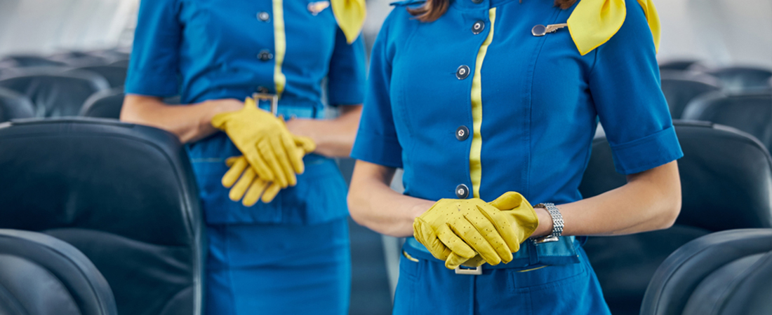 Dos TCP o azafatas de vuelo con uniforme azul y guantes amarillos formadas de pie en la cabina del avión.