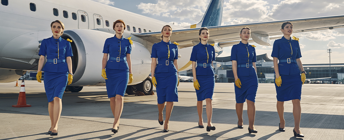 Grupo de azafatas con uniforme azul caminando en fila por la pista del aeropuerto cerca de un avión.